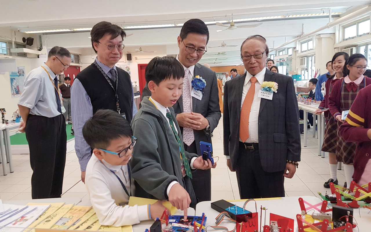 狮子会何德心小学的学生为教育局杨润雄局长及何德心副校监介 绍在常识课堂装嵌的机械人。